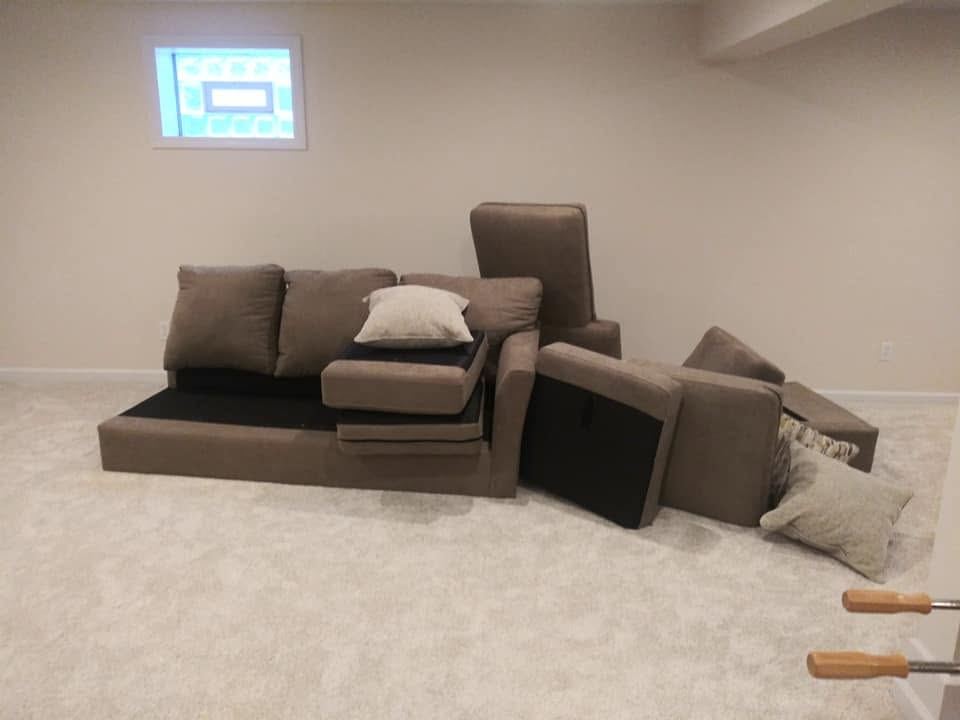 Taupe fabric sectional separated into several upholstered pieces laid out on a light carpeted floor