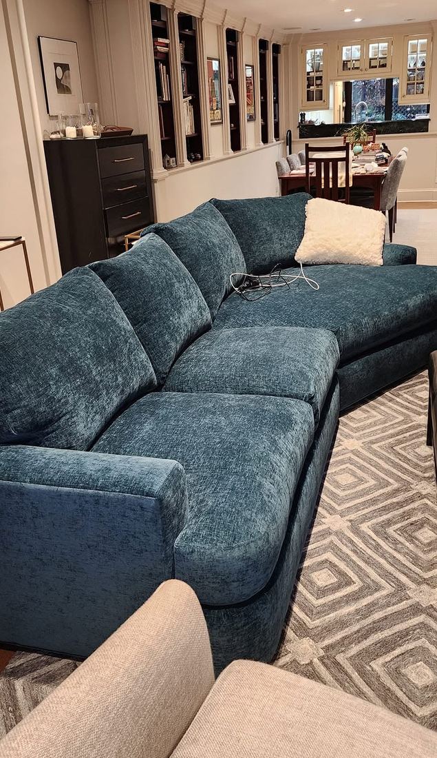 Teal velvet sectional sofa with a curved chaise end on a geometric rug in a long living room