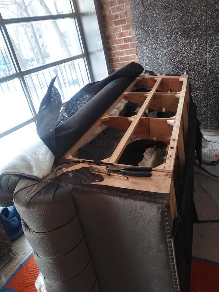 Grey tufted chesterfield with fabric peeled back to show its wood frame, pliers on top, beside a window