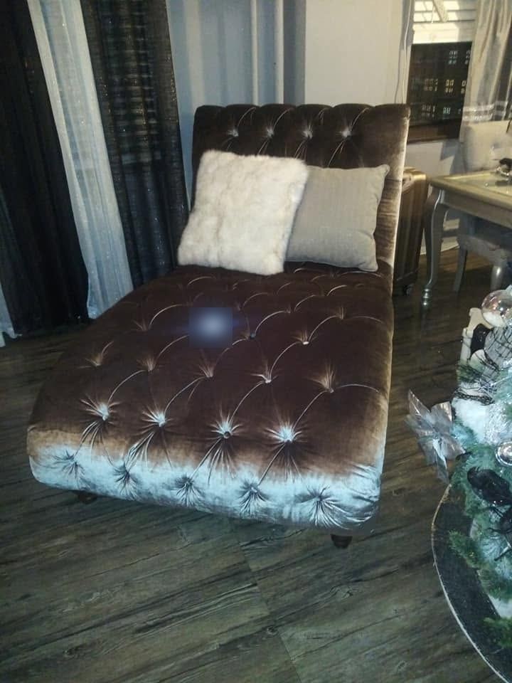 Button-tufted brown velvet chaise lounge with a white faux-fur pillow and a gray pillow on a wood floor