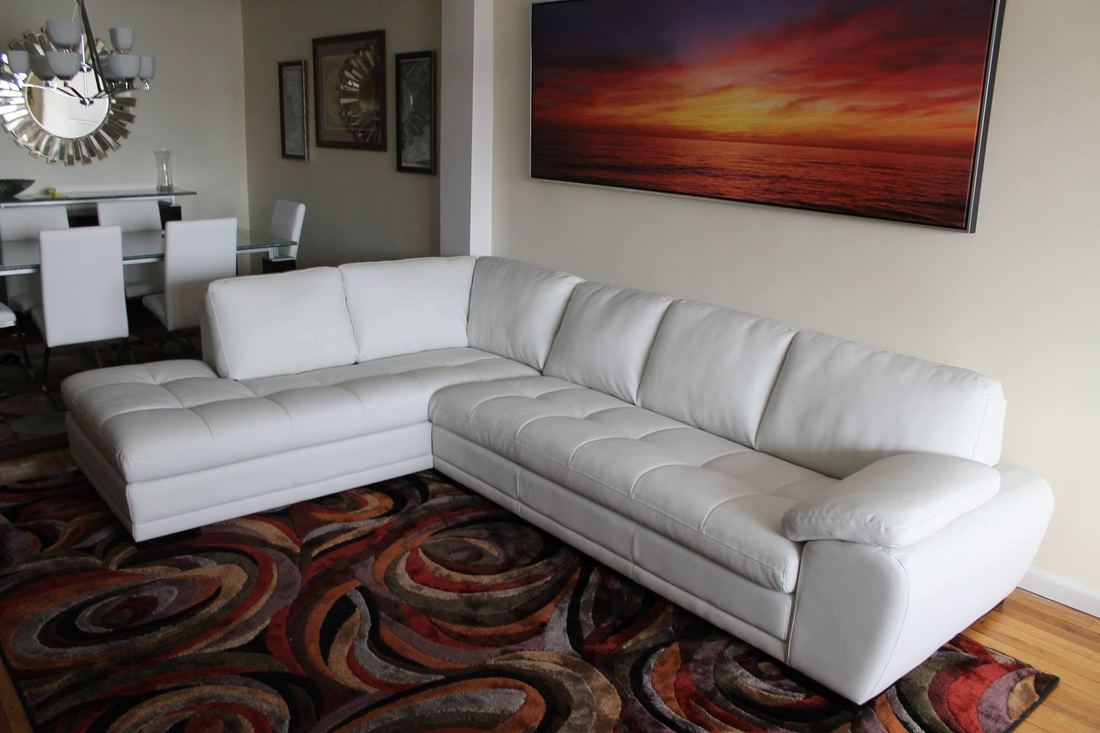 White tufted leather sectional with a left-side chaise on a multicolor swirl rug, below a large sunset print