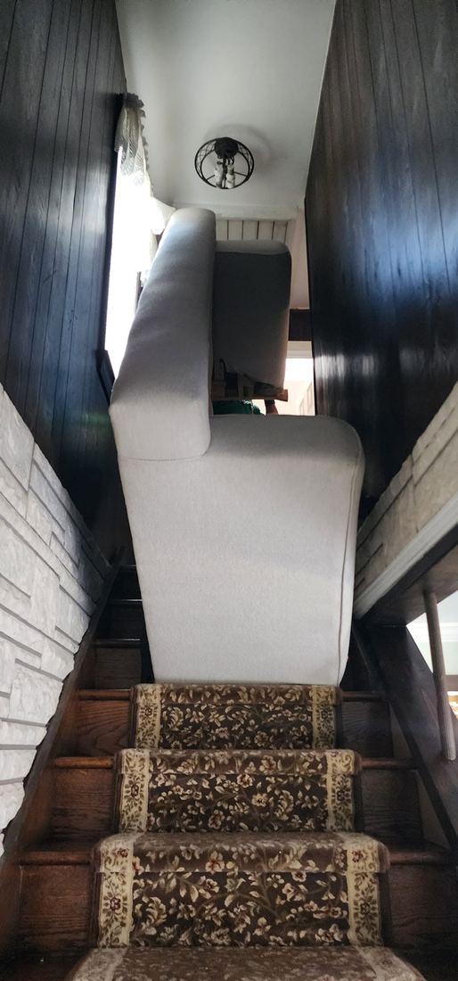 White upholstered sofa stood upright on a narrow carpeted staircase between dark wood-paneled walls