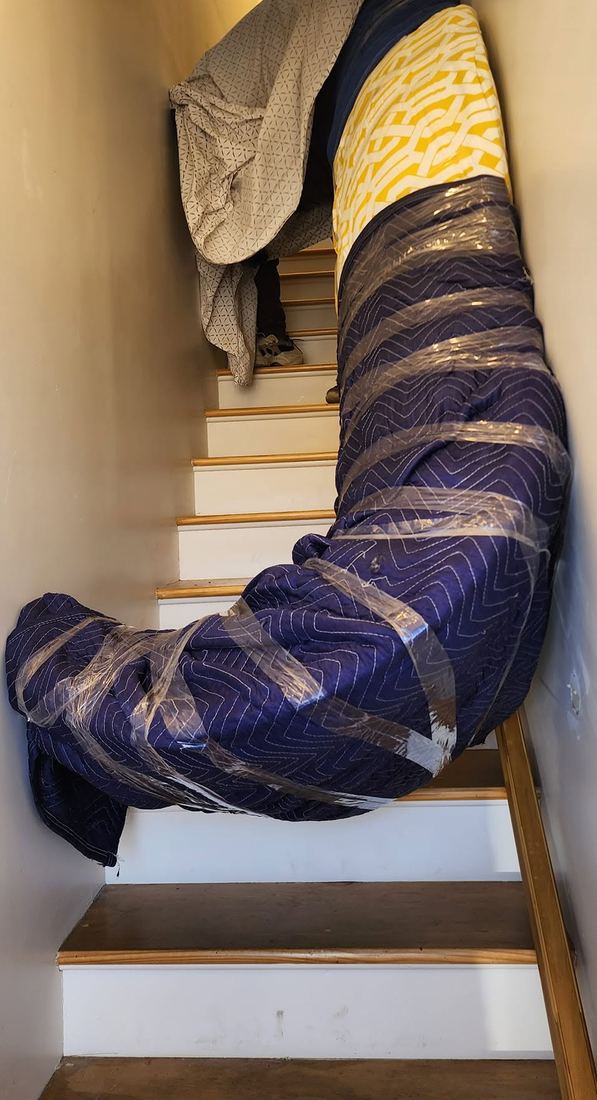 Long curved sofa wrapped in blue padded blankets and plastic wrap on a narrow white staircase