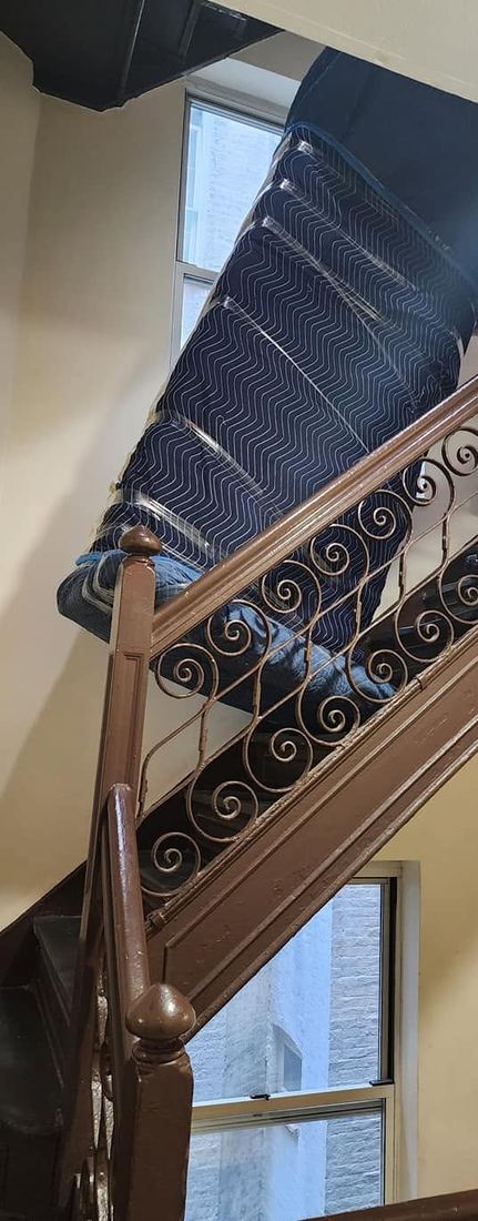 Sofa wrapped in blue padded blankets, angled over the scrolled iron railing of a stairwell