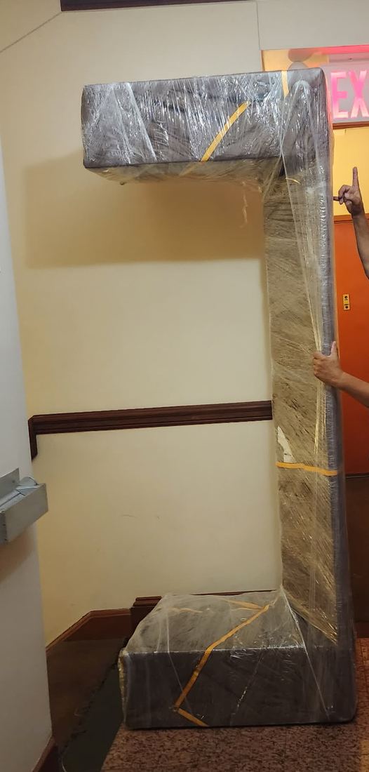 Sofa wrapped in plastic film and padding, stood upright on its end in a building lobby