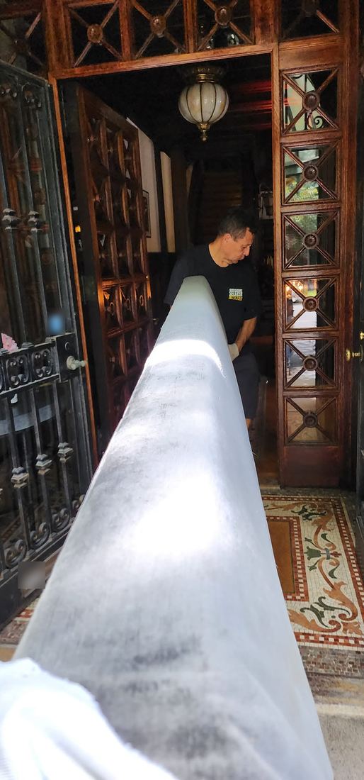 A crew member guides a long white-wrapped sofa through an ornate wooden doorway over a mosaic tile floor