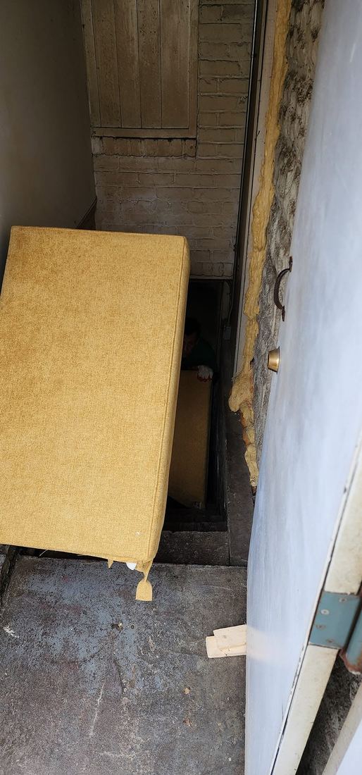 Yellow upholstered sofa section angled into a narrow brick-walled basement stairwell