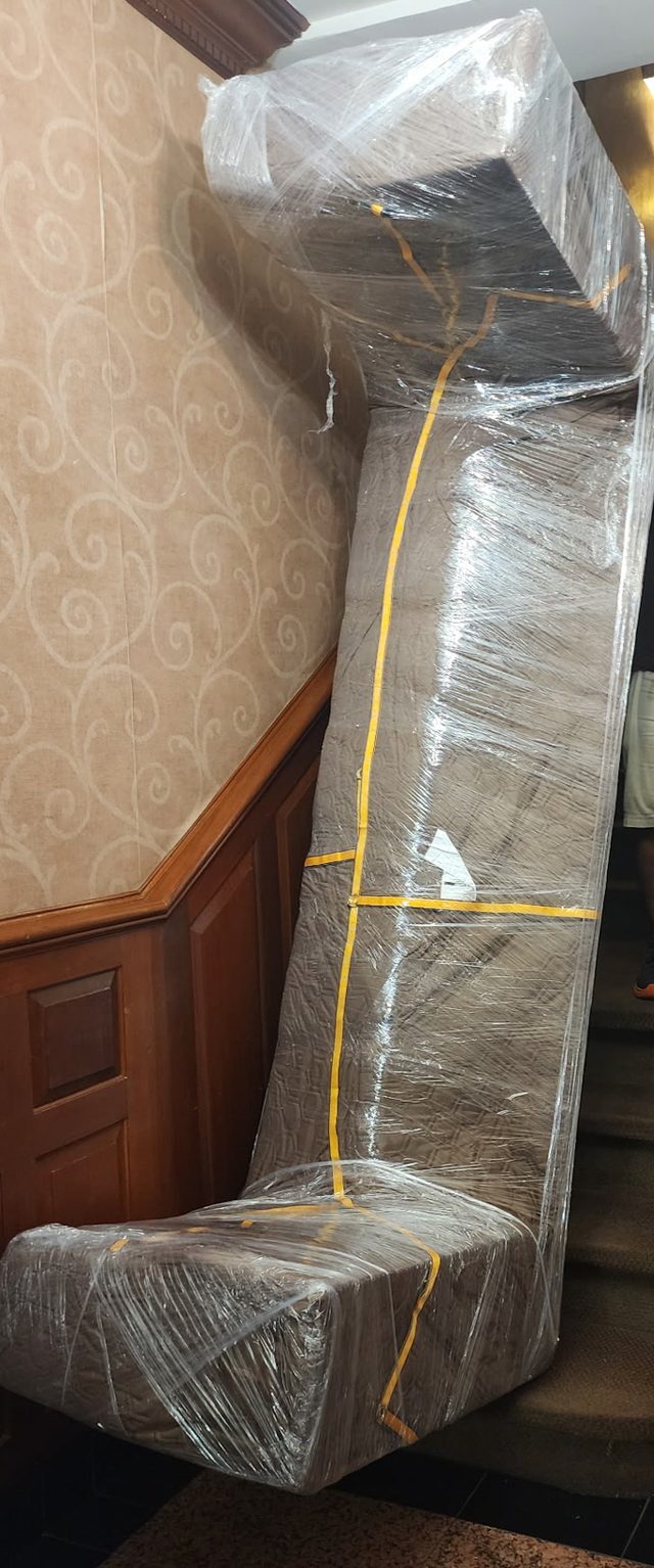 A sofa, taken apart and wrapped, carried up the stairs of an apartment building